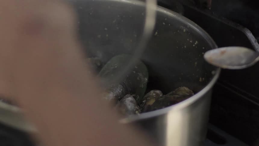 A pot with clams is being stirred then covered