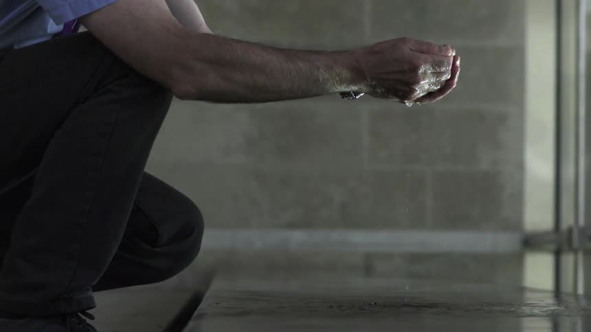 Man Putting His Hands in Reflecting Pool Water Under Calm Natural Light Outdoors.