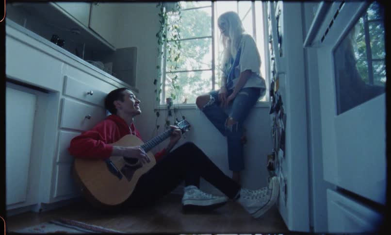 A man plays acoustic guitar in the kitchen as a woman claps along and sings