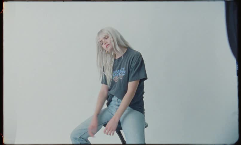Blonde girl wearing t shirt and jeans sitting on stool for a photo shoot