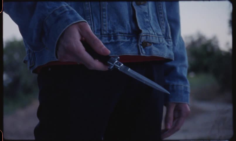 A person with a jeans jacket playing with a knife