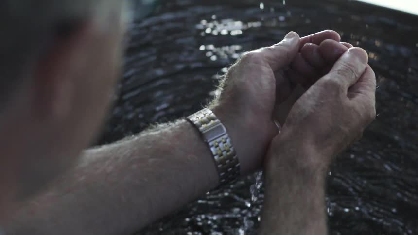 Man Cupping Water Into His Hands at Calm Outdoor Water Source in Daylight.