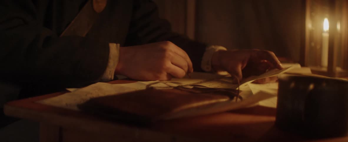 Man reads letters by candle light while taking notes