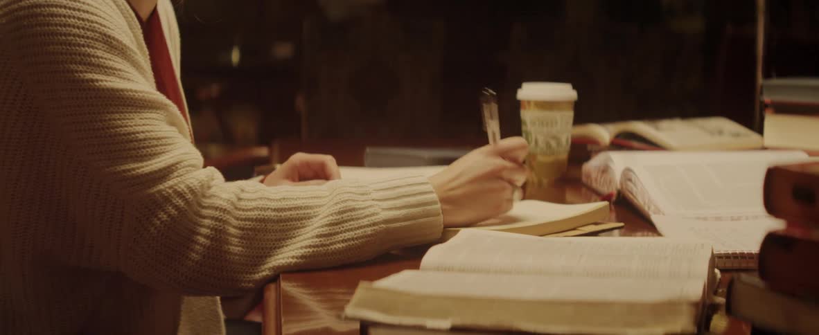 A woman sits at a desk and writes in a book and reads another book