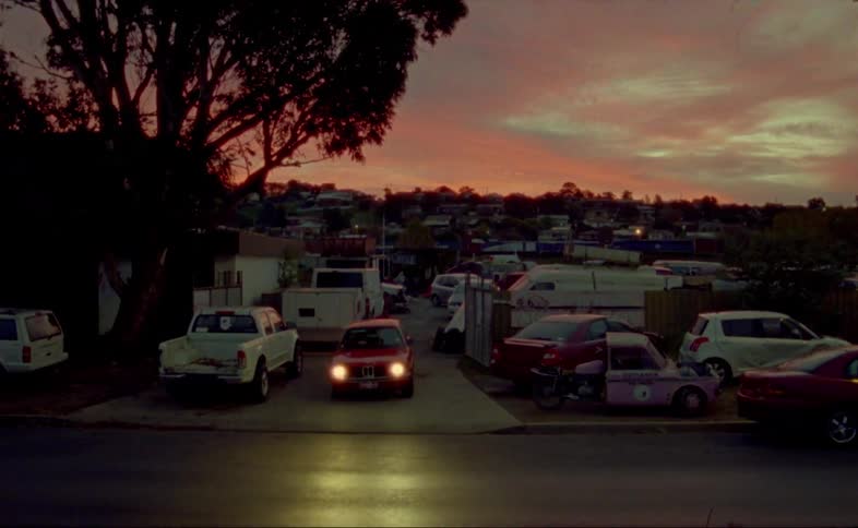 A red car speeds out of a busy parking lot