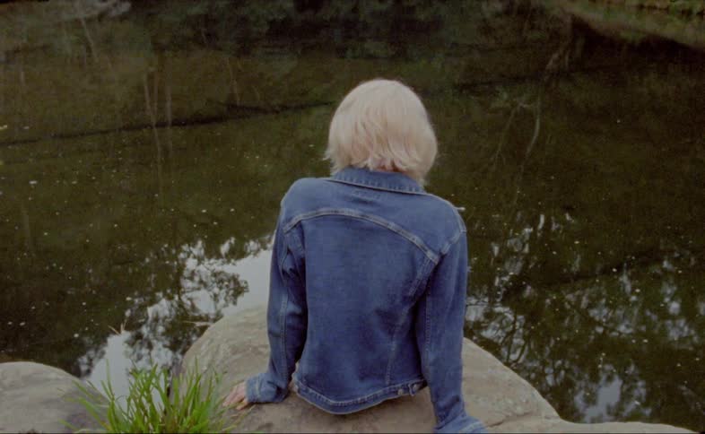A woman sits on a rock looking in to the river