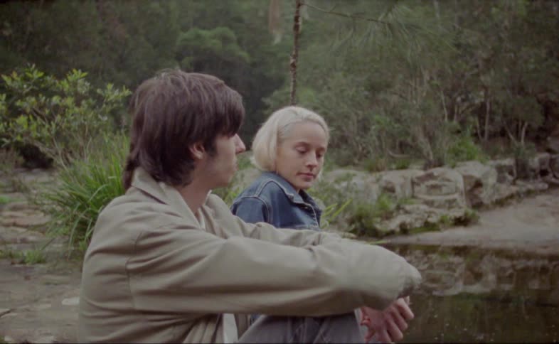A young couple sits by a lake and talks on an overcast day