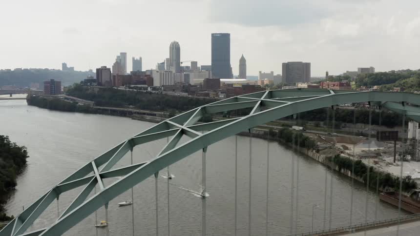 Boats pass along the river along a bridge beside a large city