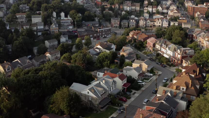 Passing over suburban neighborhood homes and streets with a city skyline on the horizon
