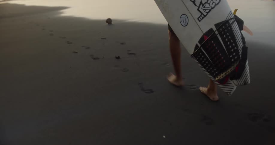 A young man carrying surf board along the beach in the evening