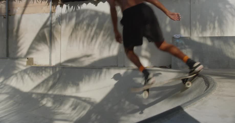 A topless skateboarder drops in from the top of a ramp on a sunny day