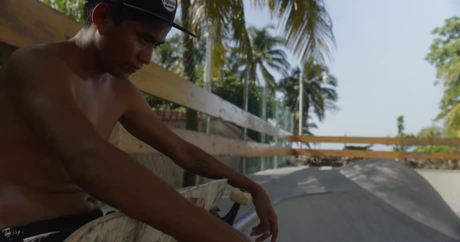 A man sits at a skate park holding his skateboard