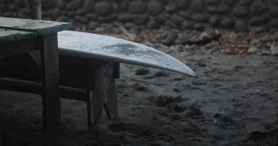 A surfboard sits on a bench in the sand