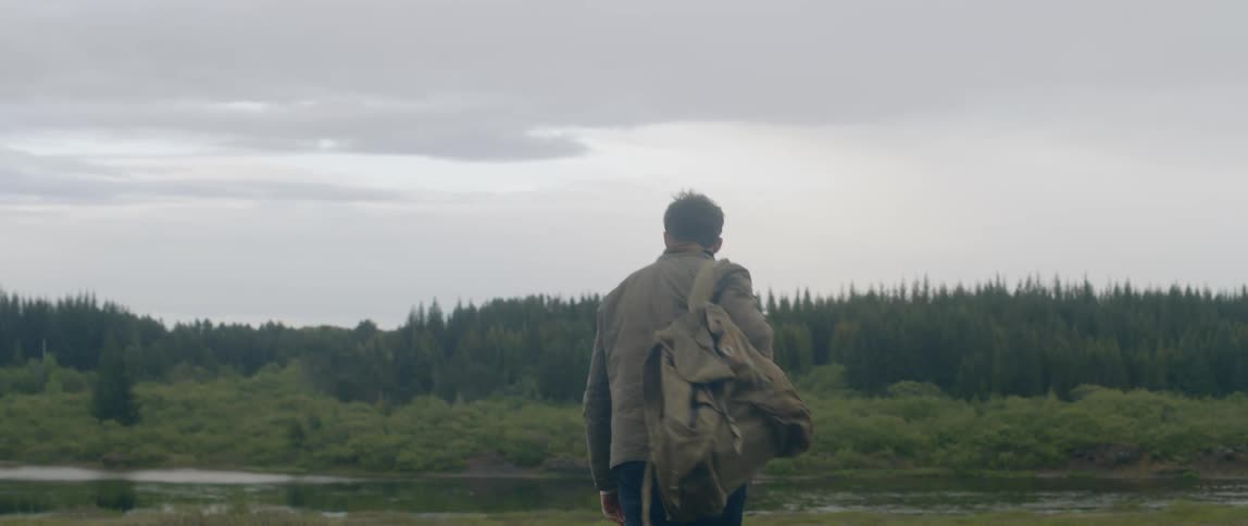 Man wearing backpack looks around and continues to walk in the forest on a cloudy day