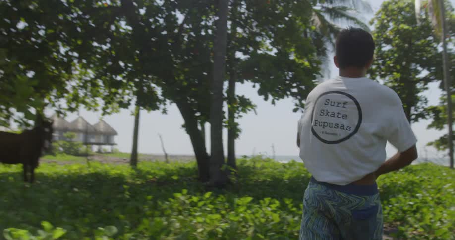 A young man puts on a shirt while walking on a trail to the beach