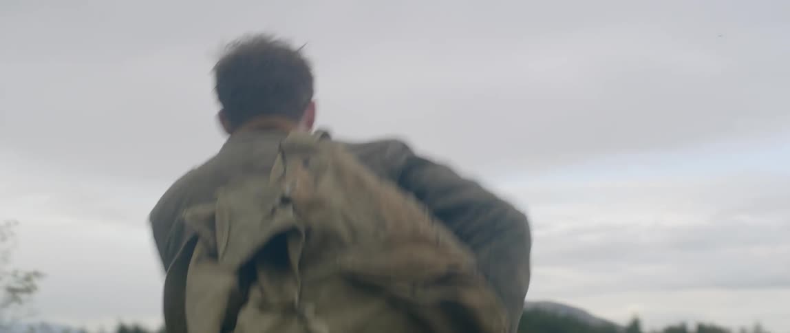 A man adjusts his backpack while walking through a field