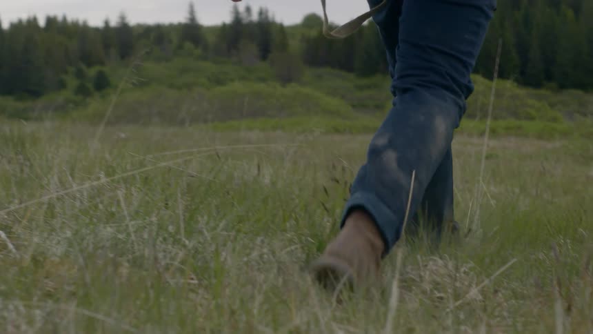 A close up shot of a man walking through a grassy field with trees off in the distance