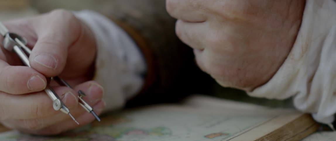 A man adjusts the spacing on a metal pencil compass before placing it on an old fashioned map of the world
