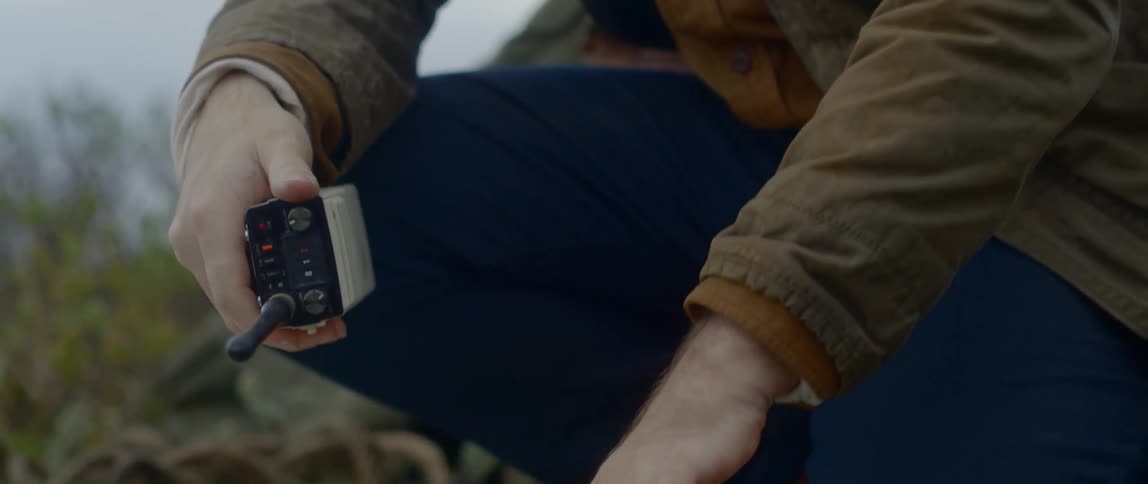 A person with a brown jacket and blue jeans tossing a walkie talkie on a piece of cardboard