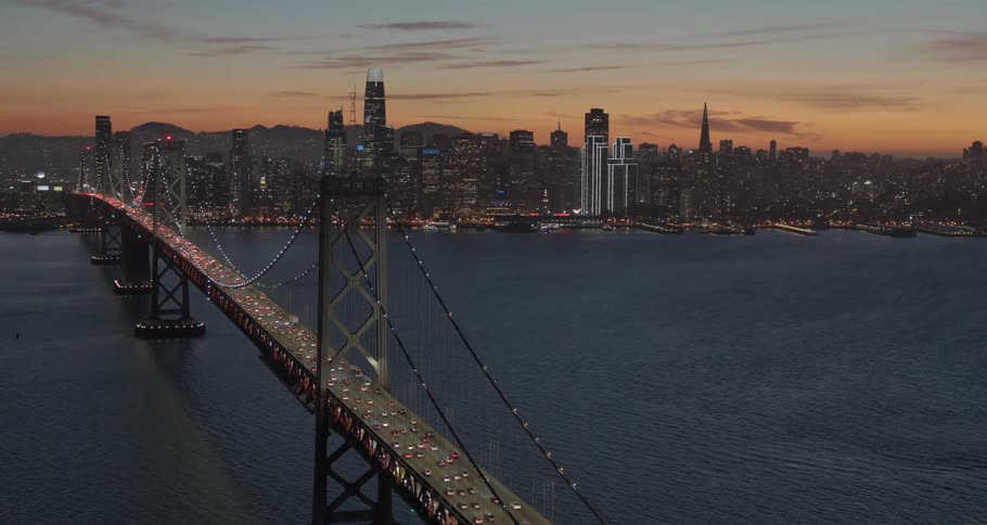 A bridge crosses a large body of water in front of a city skyline at night