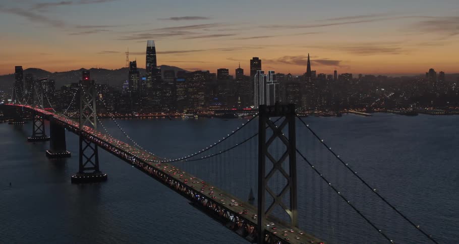 A suspension bridge over water with traffic that is near a large city