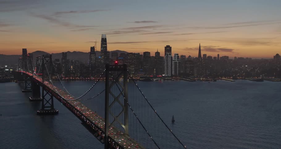 Multiple vehicles pass along a long bridge to and from a large city