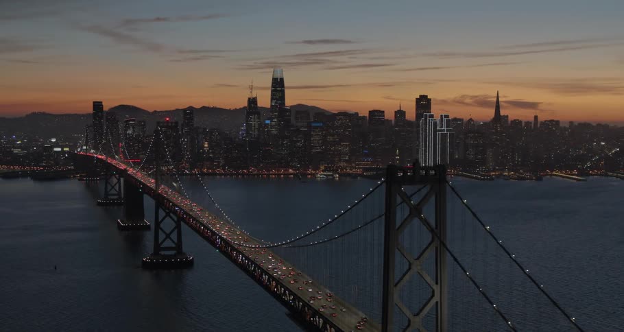 Dozens of cars cross a long bridge going in and out of a city along the water