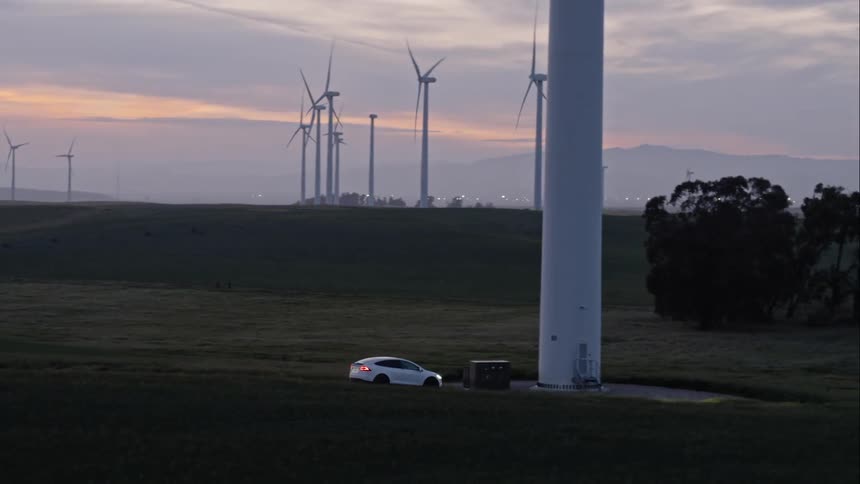 Car stopped in a road by a field and a wind farm at sunset