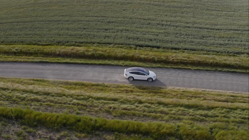 A car travels on a dirt road between crop fields on a sunny day