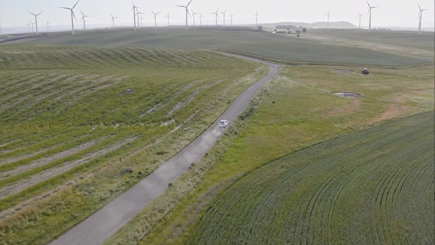 A car is driving down a dirt road near a windmill farm