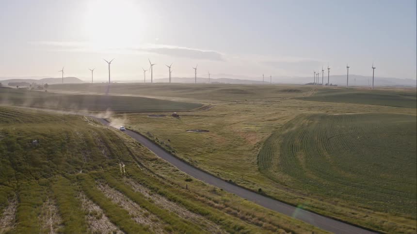 A car traveling down a narrow road on the outskirts of a wind farm