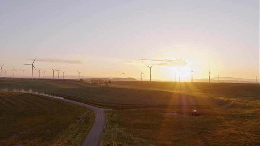 Aerial view of car driving through a field of wind turbines at dawn