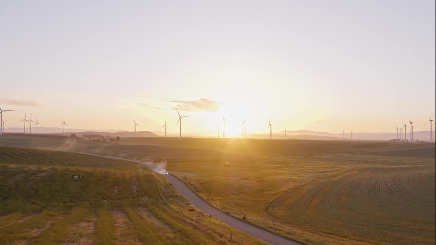 The car drives down the dirt road past the windmills