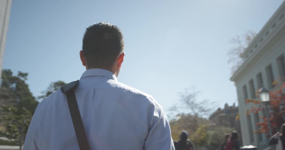 A young man carrying a bag walks along a campus