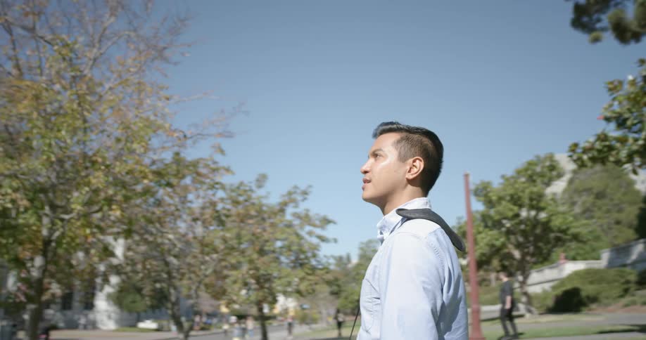 A young man stands in a grassy area between some buildings