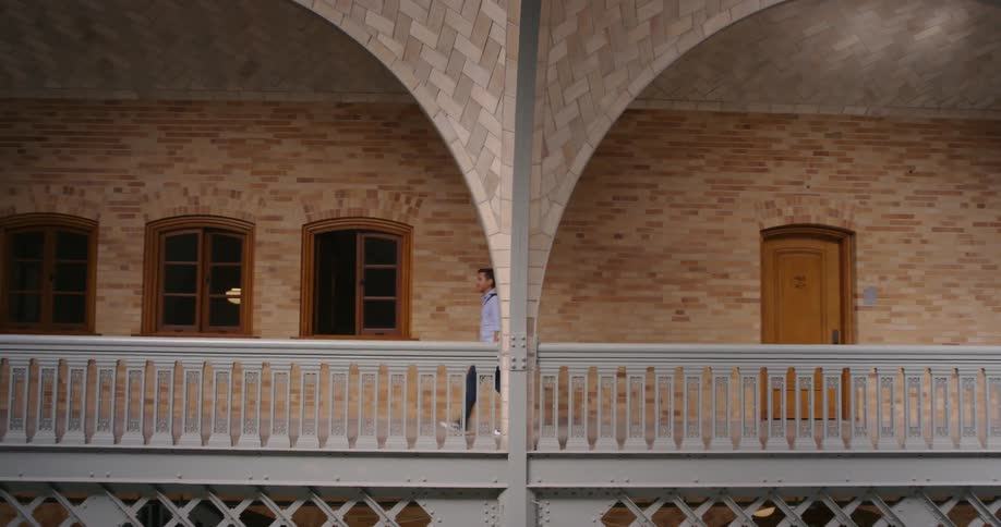 A man is walking down the hallway of a two floor building that has an atrium