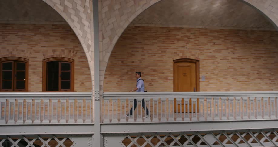 A man walking down the balcony in a building with arches