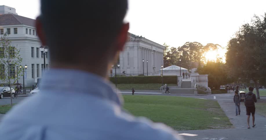 Man standing on campus with others walking around at sunset