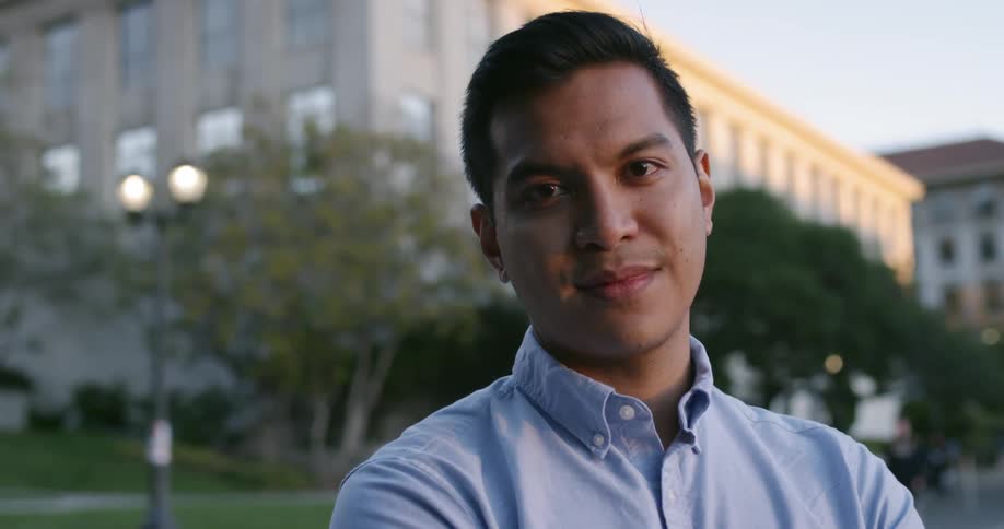 A man smiles while standing outside on a college campus