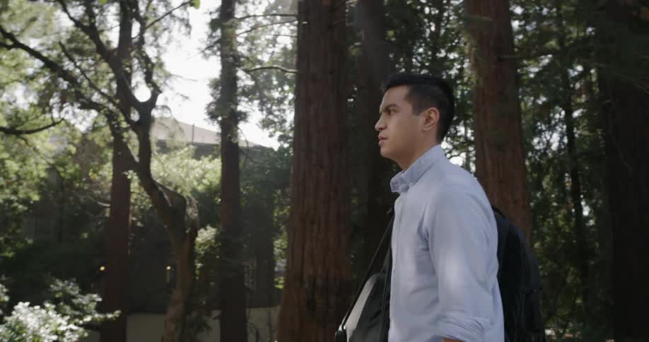 A young man walks through a forest while carrying a satchel