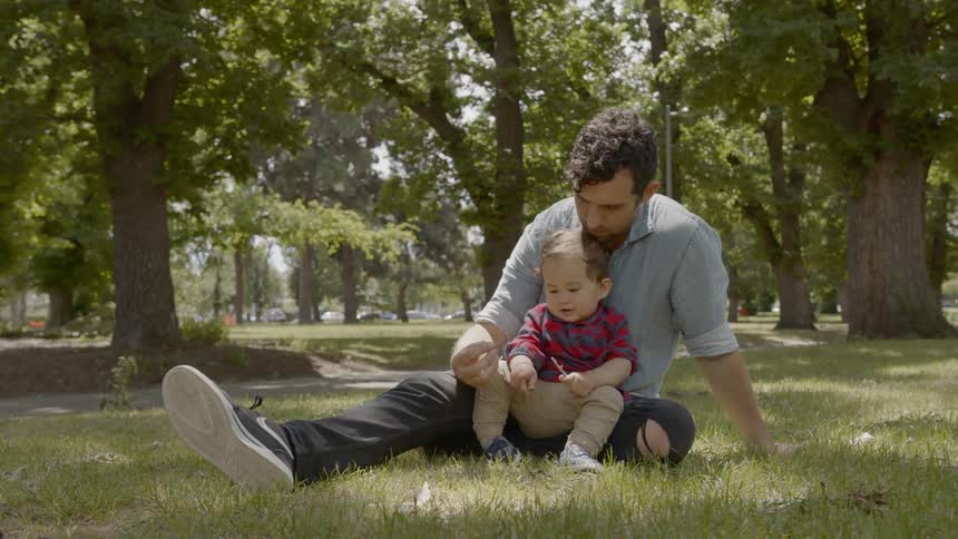 A man sits with a toddler in the park