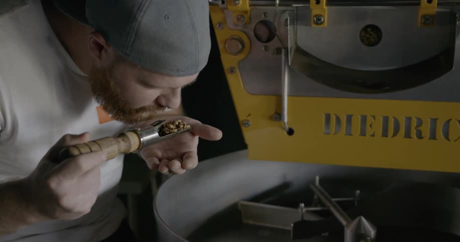 A man pulls a scoop out of a large container and smells the beans from inside