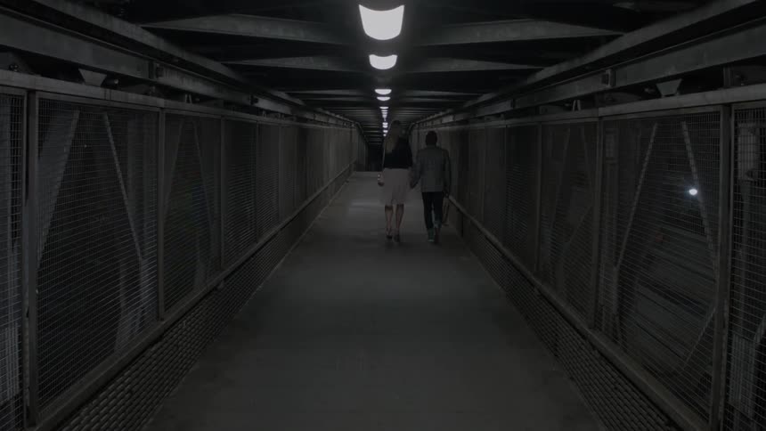 A man and woman walk through a dark tunnel with overhead lights
