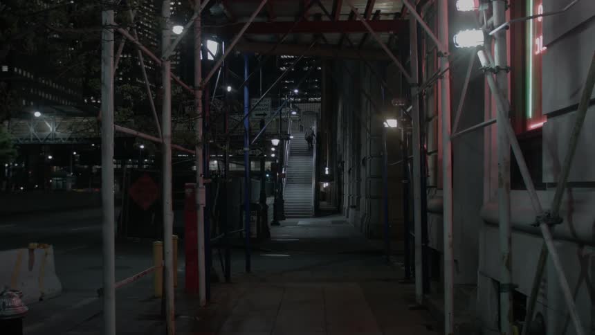 A vehicle drives beyond some dimly lit scaffolding at night