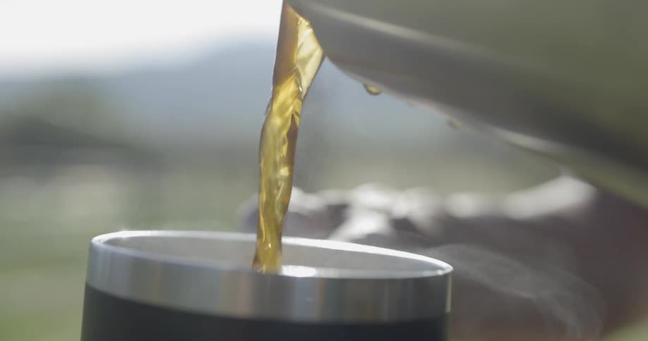 A person pours a hot liquid from one container to a cup