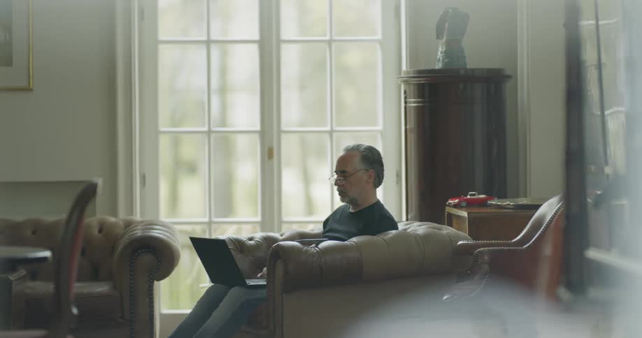 A man uses a laptop while sitting in a leather chair at home