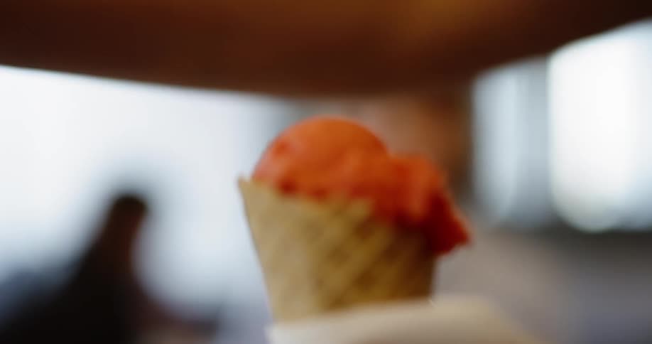 A person scoops ice cream into a cone and gives it to another person