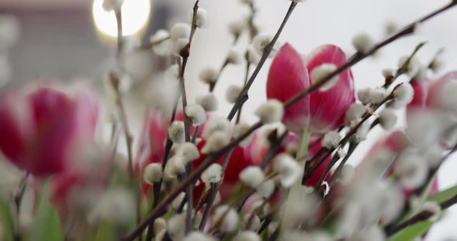 Pink tulips and branches sit in a vase in a floral arrangement
