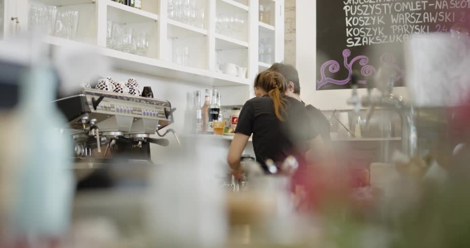 Waitress and waiter wearing black t shirt and apron work at a cafe during daylight