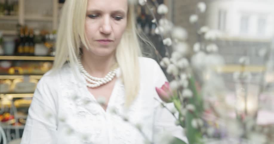 A woman is carrying flowers and willow in a vase and sets it on a surface near the camera